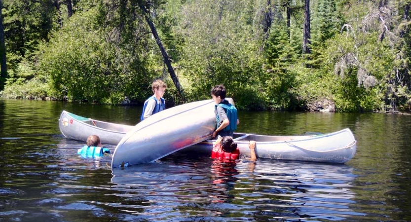 Four students wearing life jackets work together during a canoeing training exercise. 